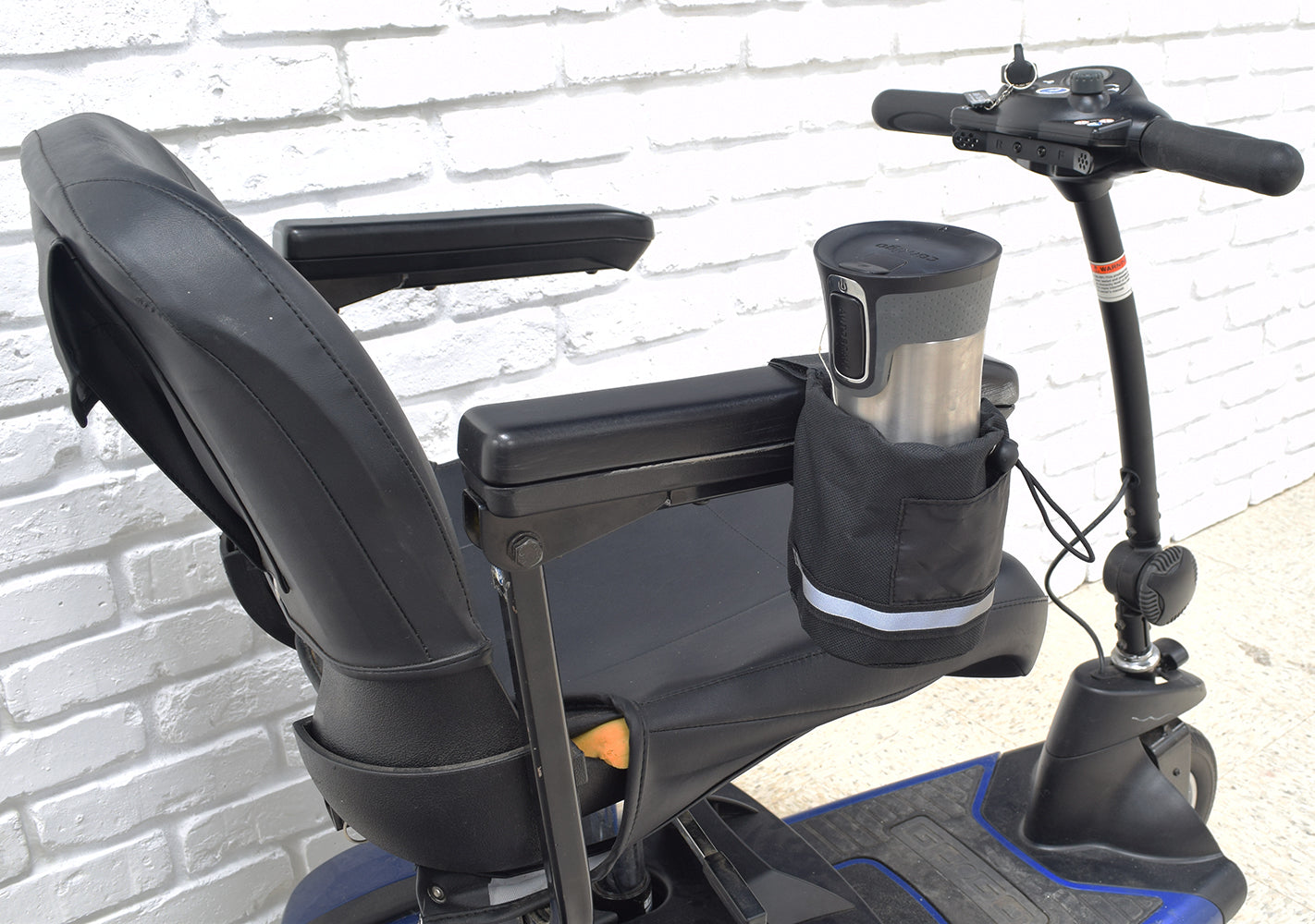 Unbreakable Universal Cup Holder for Mobility Scooters, Power Chairs, & Wheelchairs, shown attached to a black chair's armrest with a black handlebar, featuring a black fabric design and a cup holder.