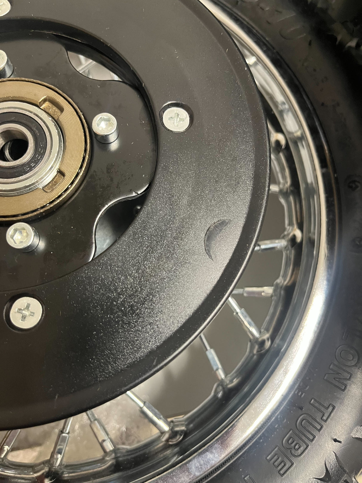 Close-up of the Rear Wheel Assembly for Razor MX500 and MX650 (Blemished), featuring the axle, rim, sprocket, tire inner tube, brake rotor, and freewheel, with visible minor blemishes on the axle bolt and sprocket.