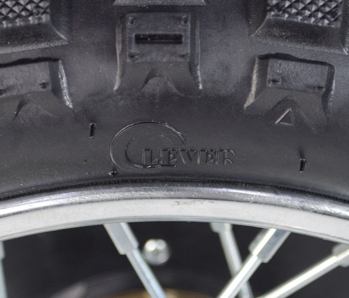 Close-up of the Rear Wheel Assembly for Razor MX500 and MX650, highlighting the tire tread, axle, rim, sprocket, and brake rotor. A screw is visible embedded in the tire.