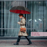 Woman holding a Golf Umbrella with Foam Handle while walking on a sidewalk. The umbrella is open, showcasing its sturdy construction and comfortable foam grip handle.