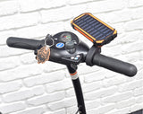 Portable Dual USB Battery Power Bank/Charger & Universal Grip Holder mounted on a scooter handlebar, featuring a solar panel for auxiliary charging and a knob for adjustments.